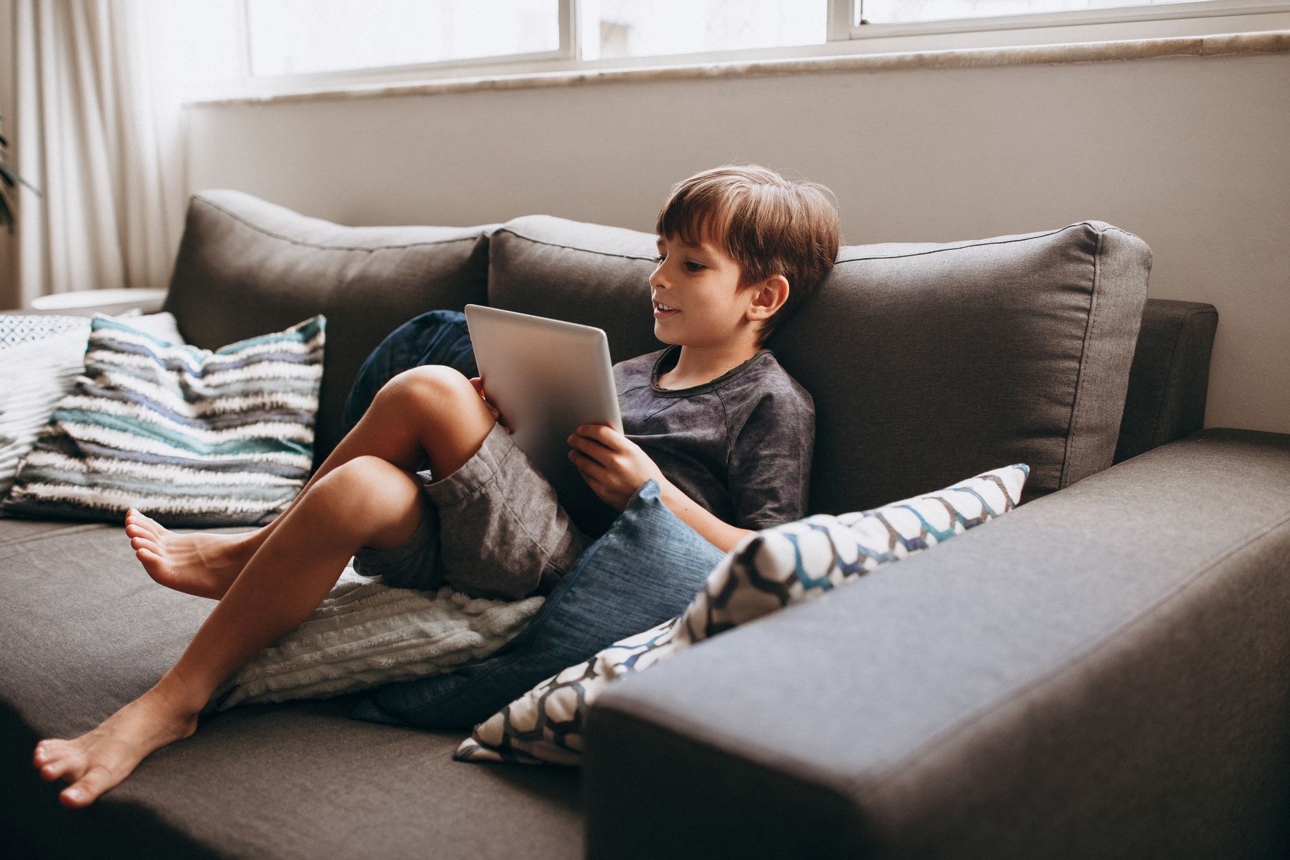 Enfant confortablement installé sur un canapé avec une tablette, dans un intérieur chaleureux.