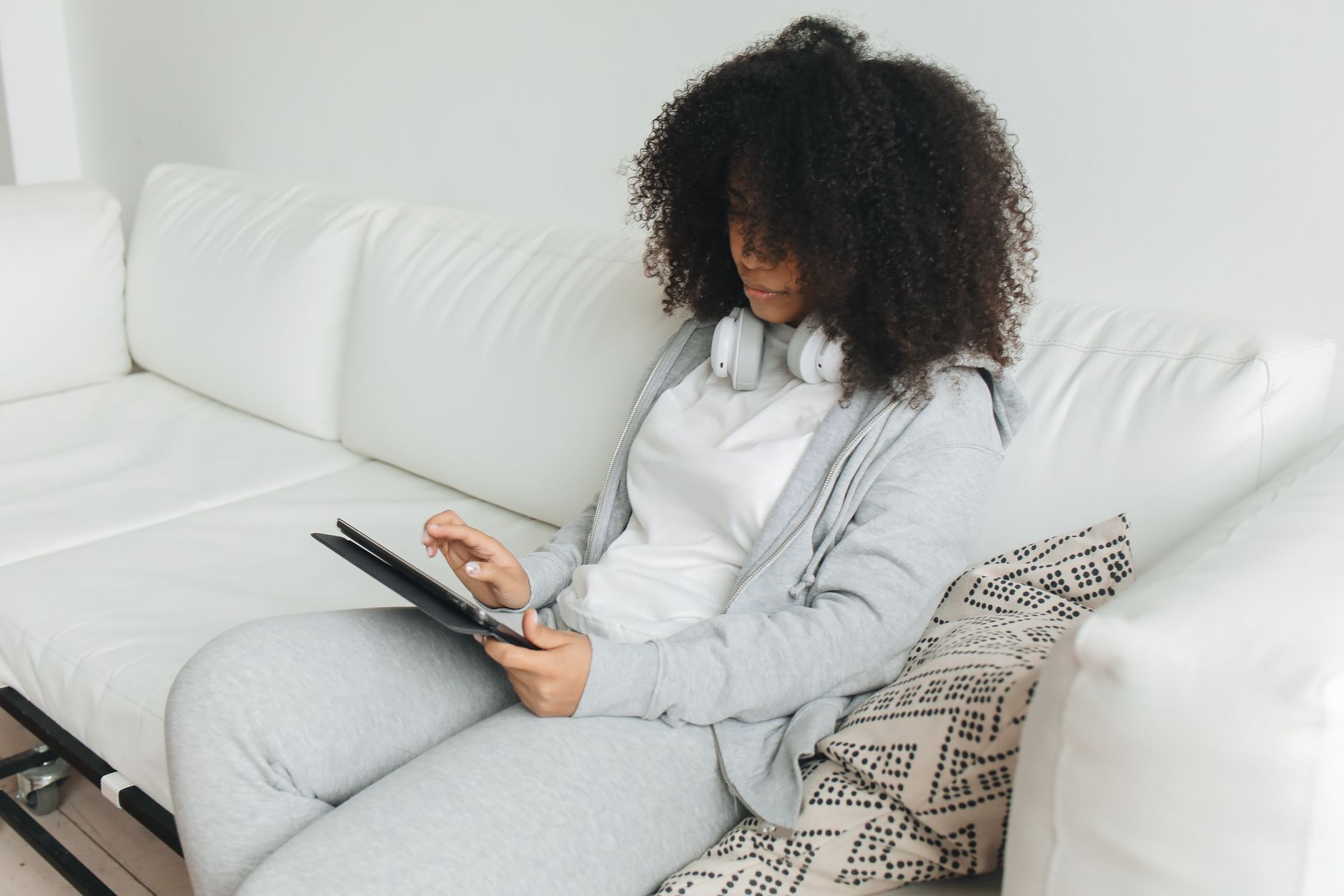 Femme portant des écouteurs, assise dans son canapé, en train de suivre une formation sur une tablette.