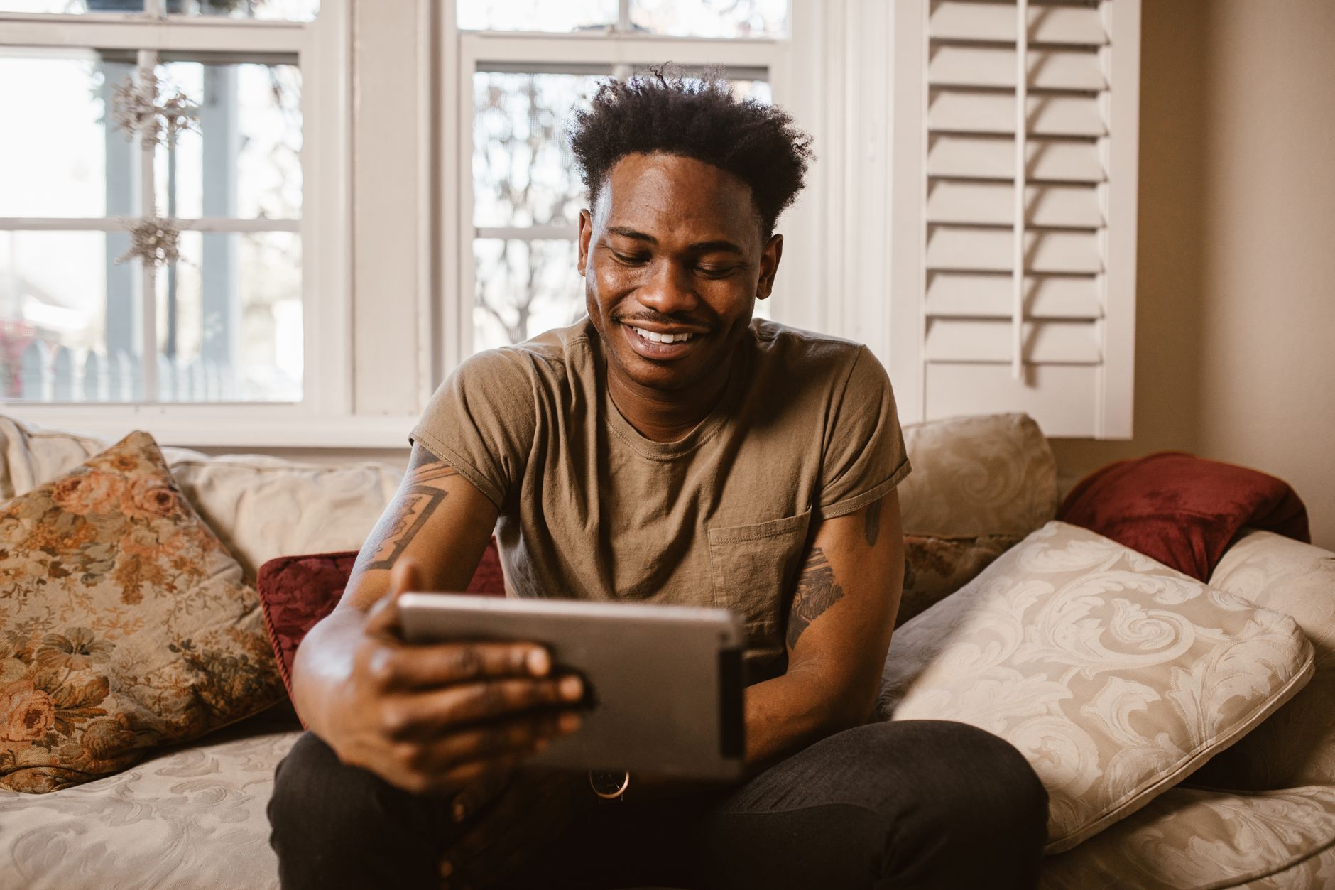 Homme souriant participant à un appel vidéo sur une tablette, confortablement installé sur son canapé.